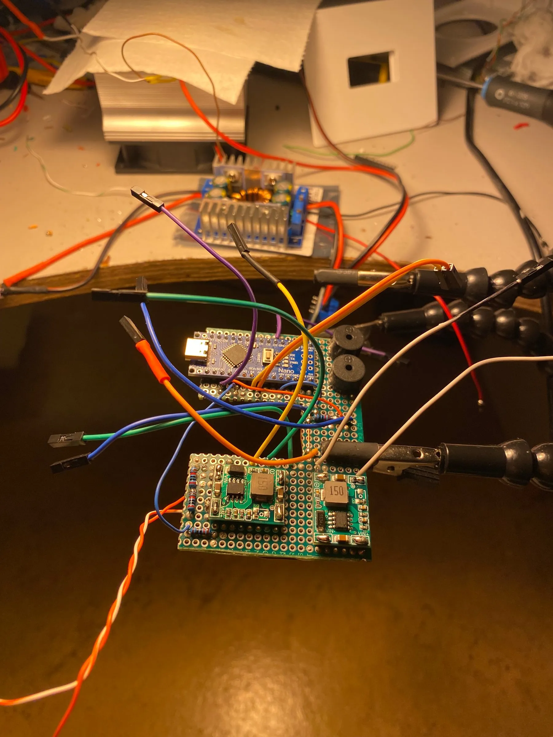 The soldered protoboard with the Arduino Nano, buck/PWM converters and buzzer, held in a helping-hands clamp.